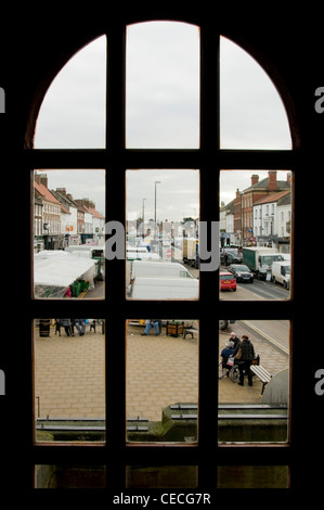 Voir à travers la vitre de la ville animée d'occupation (Northallerton High Street) le jour du marché (stands, les gens shopping, route) - North Yorkshire, Angleterre, Royaume-Uni. Banque D'Images