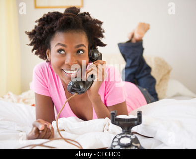 Black woman laying in bed talking on téléphone à l'ancienne Banque D'Images