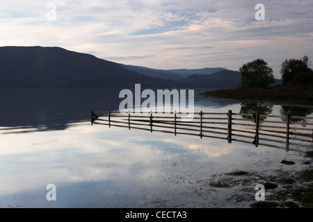 Crépuscule sur un lac calme. Une clôture est reflétée dans l'eau comme il est immergé dans l'eau progressivement. Banque D'Images