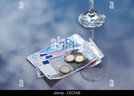 Verre de vin vide avec des billets et des pièces sur un plateau en verre table de café. Banque D'Images