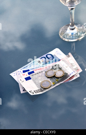 Verre de vin vide avec des billets et des pièces sur un plateau en verre table de café. Banque D'Images