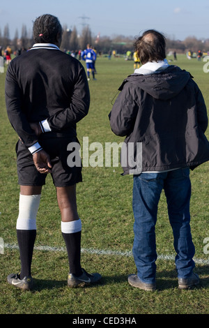 Un arbitre et un coach se tenir ensemble, regarder un match de football de ligue Dimanche, l'arrière-plan est une correspondance, Hackney Marshes, Londres. Banque D'Images