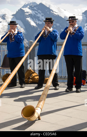 Close up portrait of horizontal de trois hommes Suisse vêtements traditionnels à jouer du cor des Alpes avec les Alpes Suisses derrière eux. Banque D'Images