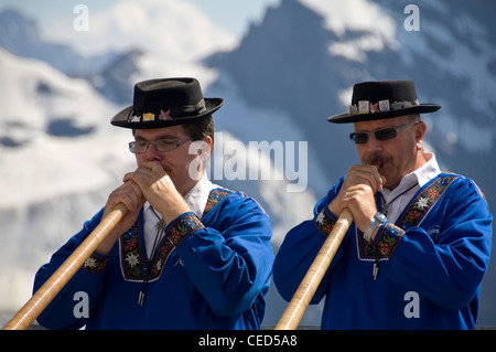 Close up portrait of horizontal de deux hommes habillés traditionnellement Swiss jouer du cor des Alpes avec les Alpes Suisses derrière eux. Banque D'Images