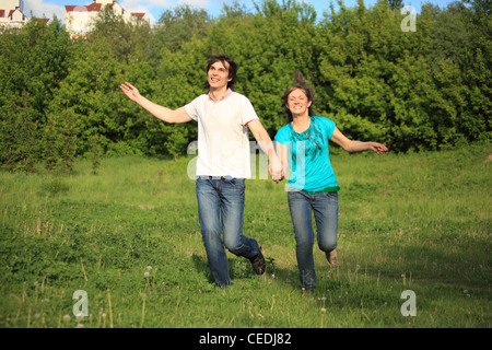 Smiling young couple s'exécute, en gardant pour les mains, de l'herbe dans park Banque D'Images