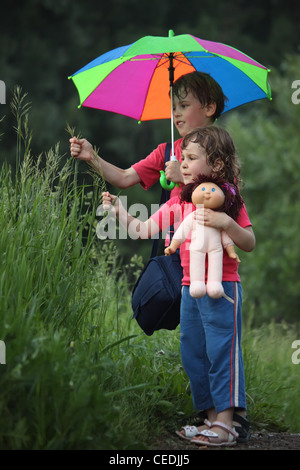 Garçon et fille sous parapluie dans l'herbe la déchirure du parc Banque D'Images