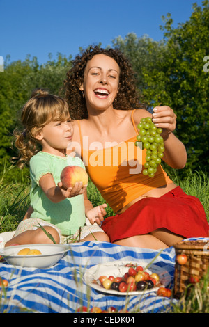 Jolie petite fille et les jeunes femmes se tient en main les fruits on picnic Banque D'Images