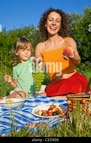 Jolie petite fille et les jeunes femmes se tient en main les fruits on picnic Banque D'Images