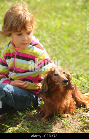 Petite fille avec teckel est assis sur l'herbe Banque D'Images