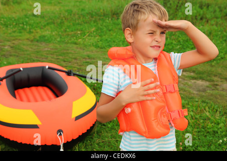 Garçon veille et bateau gonflable sur la pelouse Banque D'Images