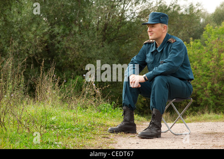 L'homme militaire assis sur la chaise de camping en plein air Banque D'Images