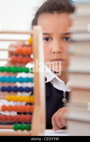 Une belle jeune mixed race African American girl dans une salle de classe avec une pile de livres en face d'elle à l'aide d'un abaque Banque D'Images