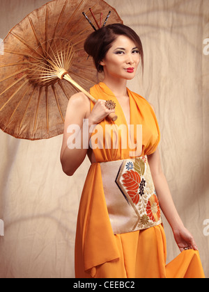 Belle asiatique femme portant une robe orange stading avec un parapluie dans sa main Banque D'Images