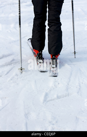 Les jambes d'un skieur avec des bâtons de ski, pantalon de ski noir et rouge chaussures de ski sur les pistes, vus de derrière. Banque D'Images