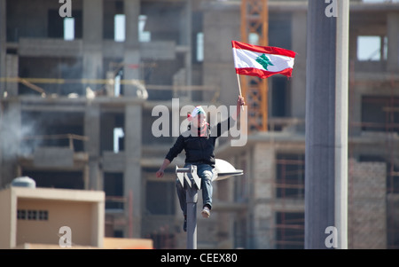 Jeune homme libanais sur haut de réverbère vagues drapeau que la masse rassemblement politique à la Place des Martyrs, à Beyrouth, Liban Banque D'Images