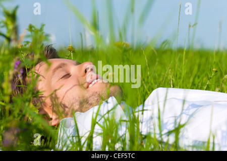 Jeune homme allongé sur une pelouse ou prairie en été et est rêver ou dormir Banque D'Images