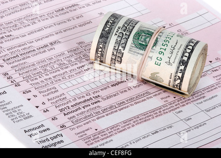 Un rouleau de trésorerie USD assise sur un chèque en blanc, rose sous forme d'impôt IRS Banque D'Images