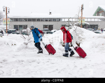 Deux personnes faisant glisser valises dans la neige, Bourg St Maurice, France Banque D'Images