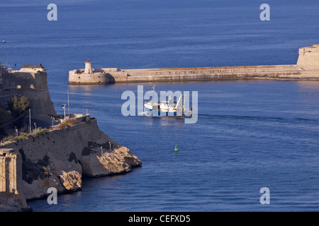 Le phare à la fin de Point Ricasoli à l'entrée du Grand Port avec un chalutier vers la mer au coucher du soleil Banque D'Images