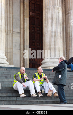 Un protestataire Occupy London parler aux travailleurs de la construction qui sont assis en train de déjeuner sur l'entrée principale étapes de St Paul's Banque D'Images