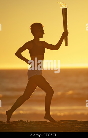 Une femme s'exécutant sur la plage avec une simulation de relais aux Jeux olympiques de chalumeau. Banque D'Images