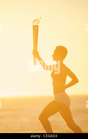 Une femme s'exécutant sur la plage avec une simulation de relais aux Jeux olympiques de chalumeau. Banque D'Images