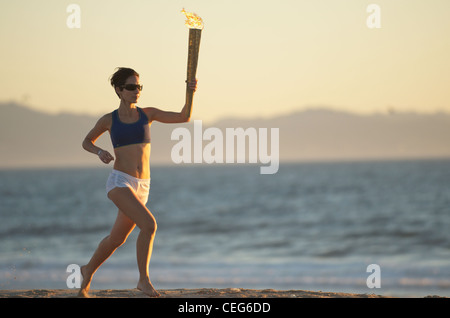 Une femme s'exécutant sur la plage avec une simulation de relais aux Jeux olympiques de chalumeau. Banque D'Images