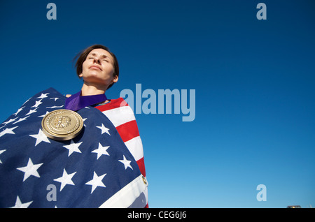 Portrait d'une femme enveloppée dans un drapeau américain portant une simulation d'une médaille d'or olympique. Banque D'Images