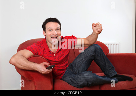 Seul heureux et excité l'homme jouissant de regarder la télévision sur le mur de poing à l'air de fête. Banque D'Images