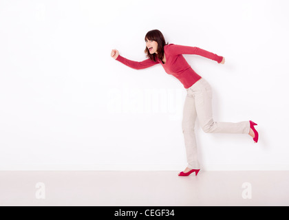 Belle et heureuse femme simulant la course elle contre un mur blanc Banque D'Images