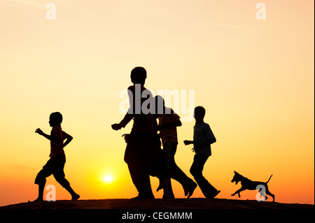 Silhouette de jeune Indien enfants courant et jouant avec un chiot. L'Inde Banque D'Images