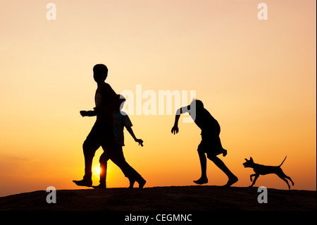 Silhouette de jeune Indien enfants courant et jouant avec un chiot. L'Inde Banque D'Images