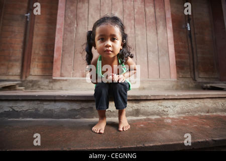 Portrait of cute Asian enfant femelle en T-shirt vert assis sur rue et looking at camera Banque D'Images