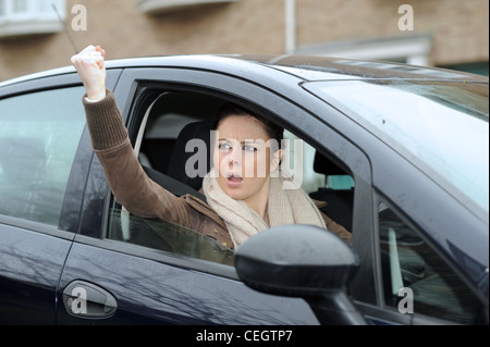 Une femme dans ses années 20s en colère conduisant une voiture avec la route Rage criant sur d'autres automobilistes au Royaume-Uni (posé par le modèle) Banque D'Images