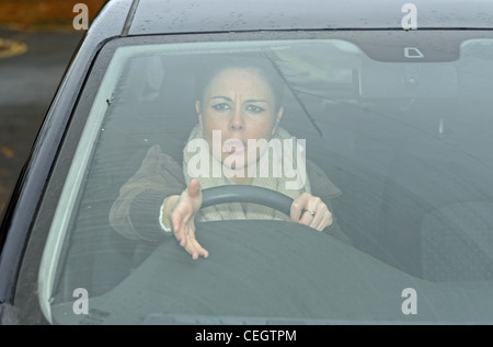 Une femme dans ses années 20s en colère conduisant une voiture avec la route Rage criant sur d'autres automobilistes au Royaume-Uni (posé par le modèle) Banque D'Images