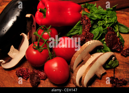 Champignons portabella, tomates mûries sur pied, basilic frais, aubergines et tomates séchées au soleil sur une planche à découper. Banque D'Images