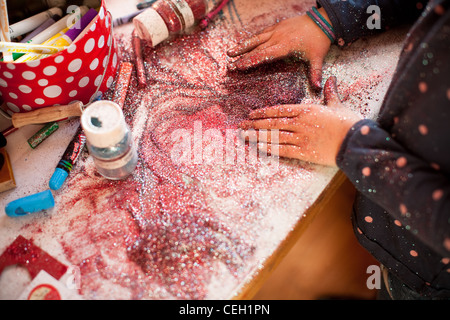 Sept ans, fille de jouer avec un tas de violet et rose glitter valentine lors d'un projet artistique, United States Banque D'Images