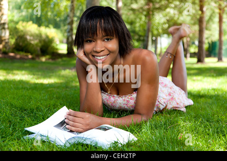 Outdoor portrait of young african american woman couché sur l'herbe la lecture d'un livre Banque D'Images