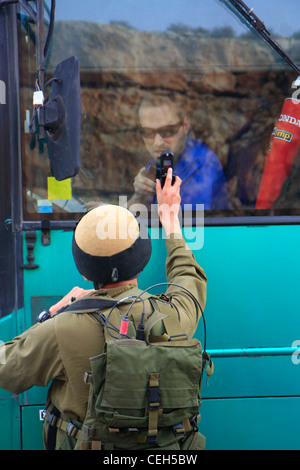 Un soldat israélien utilise un téléphone cellulaire pour communiquer à travers une fenêtre avec un chauffeur de bus Egged. Banque D'Images