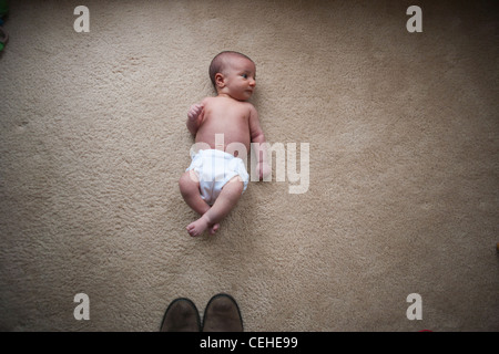 Un bébé nouveau-né fille portant sur le sol en face de la pointe des chaussures, montrant la petite taille de l'enfant. Banque D'Images