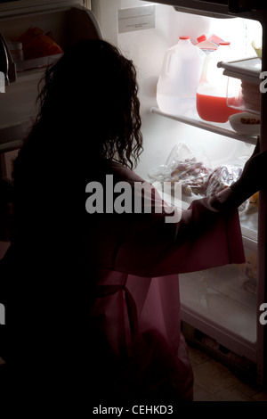 Silhouette d'embonpoint ethnic African American Woman in pajama accroupis par réfrigérateur à la recherche de nourriture dans la nuit. Banque D'Images