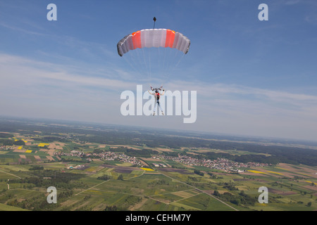 Parachutiste sous voile est survolant des champs verts dans le ciel bleu et s'apprête à enregistrer des terres sur le terrain. Banque D'Images