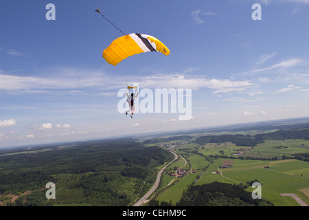 Parachutiste sous voile vole dans le ciel bleu avec quelques petits nuages et elle se prépare à enregistrer des terres sur le terrain. Banque D'Images