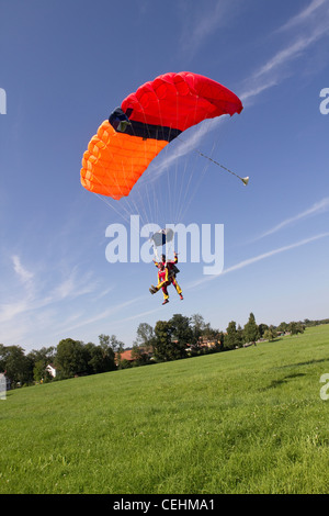 Couple parachutiste sous voilure volent dans plus de champs verts dans le ciel bleu et se préparent à enregistrer des terres sur le terrain. Banque D'Images