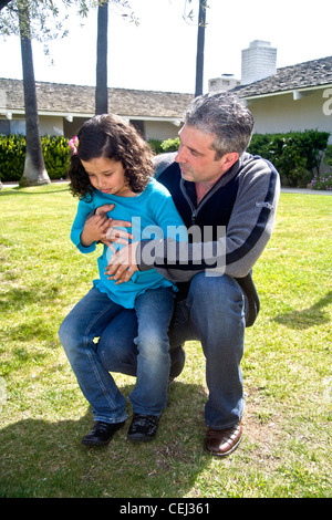 Un enfant de cinq ans Egyptian-American fille est réconforté par son père alors qu'elle grimace de douleur d'un mal d'estomac Banque D'Images