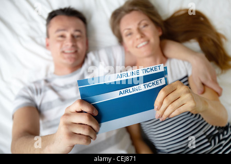 Happy young couple lying on bed with billets d'avion dans les mains Banque D'Images