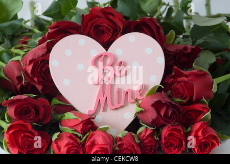 Coeur rose en bois avec les mots "Be Mine" sur un lit de roses rouges Banque D'Images