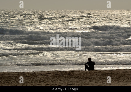 Lone surfer sitting on beach looking at sea Banque D'Images