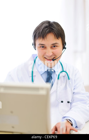 Smiling medical doctor avec Travail avec casque sur un pc Banque D'Images