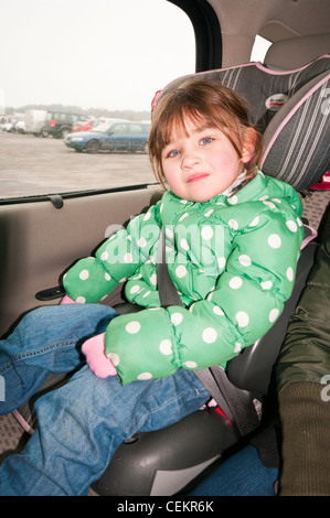 Jeune enfant portant une ceinture de sécurité sur le siège enfant sur le siège arrière d'une voiture Banque D'Images